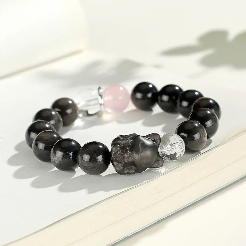 Silver stone crystal bracelet with diamond-shaped fox, cat head, and planet charms on white background.