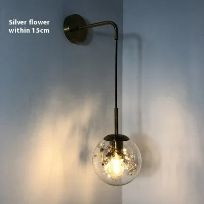 Glass wall lamp with golden flower finish and 15cm diameter, mounted beside bed with LED illumination