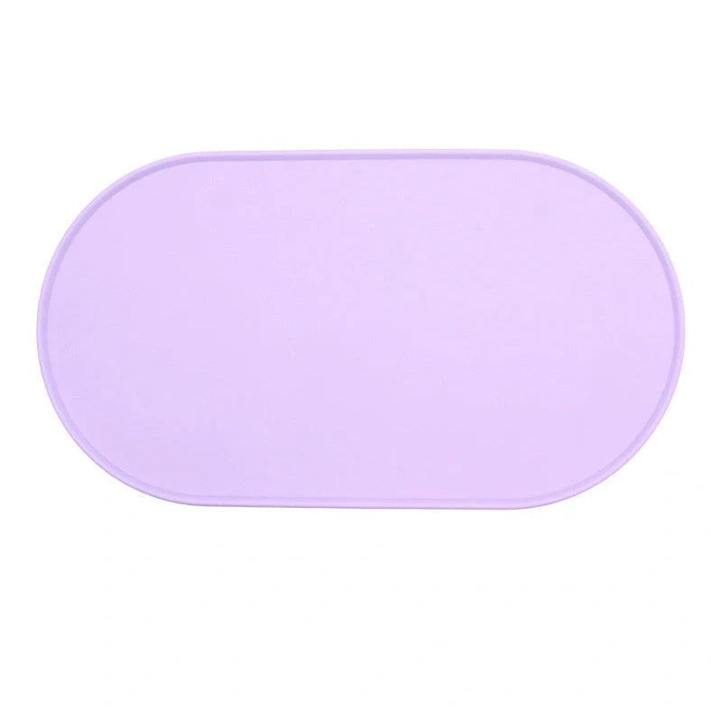 Green silicone cat feeding placemat with raised edges on wooden floor containing water bowl