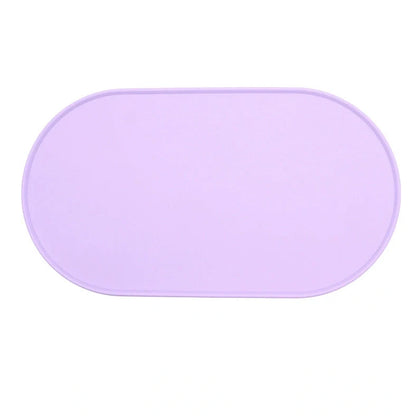 Green silicone cat feeding placemat with raised edges on wooden floor containing water bowl