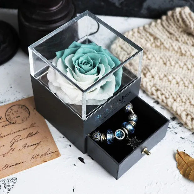 Blue and pink eternal flower gift box with roses and carnations on a table.