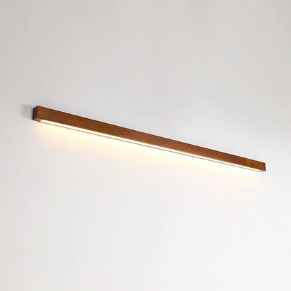 Slim walnut-colour wooden strip wall lamp with integrated LEDs mounted on a plain wall.