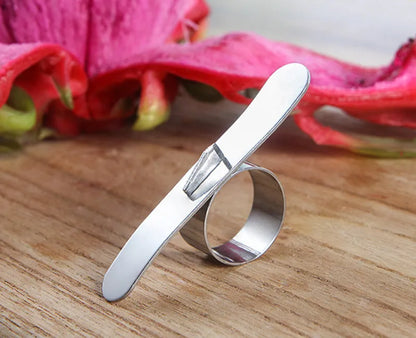 Silver stainless steel citrus fruit peeler with a ring handle on a wooden surface.