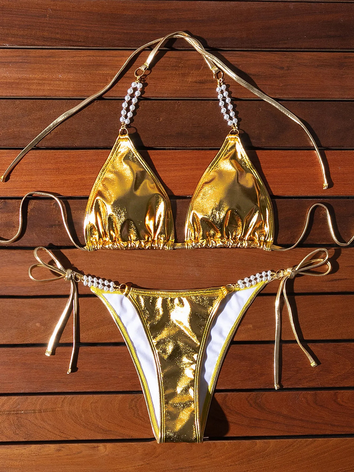 Gold women's halter neck bikini with lace-up front and pearl chain decoration on a solid background.