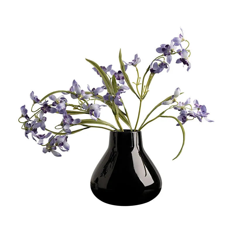 Black ceramic vase with round belly design and two white artificial orchid stems on wooden table