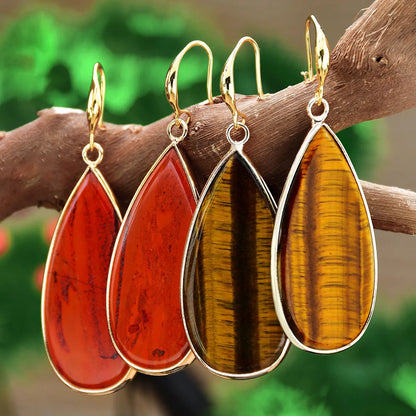 Close-up of long, polished tigereye stone drop earrings with a fishhook clasp on a neutral background.