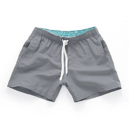 Man wearing straight-leg polyester beach shorts in a bright colour on the sand.