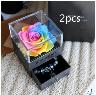 Blue and pink eternal flower gift box with roses and carnations on a table.