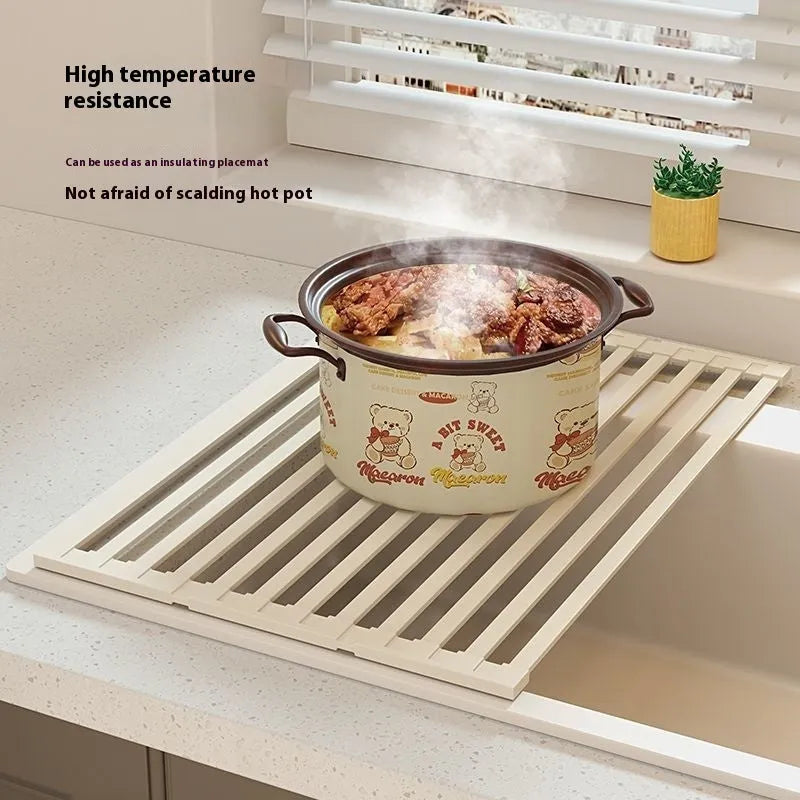A milky white foldable stainless steel kitchen draining rack collapsed flat beside a kitchen sink.