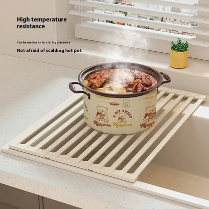 A milky white foldable stainless steel kitchen draining rack collapsed flat beside a kitchen sink.