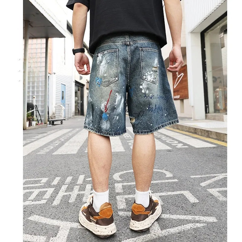 Blue denim men's shorts with ripped knees and graffiti design, featuring a straight leg and zipper fly.