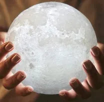 3D printed white moon lamp glowing on a wooden stand, showing detailed crater texture on its surface.