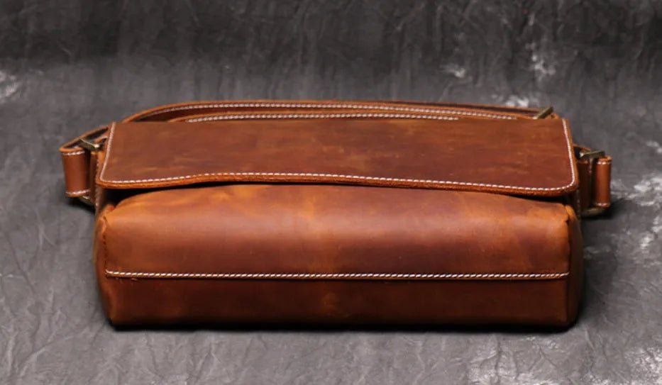 Vintage brown leather men's messenger bag with a cover flap, showing the internal document and phone pockets.