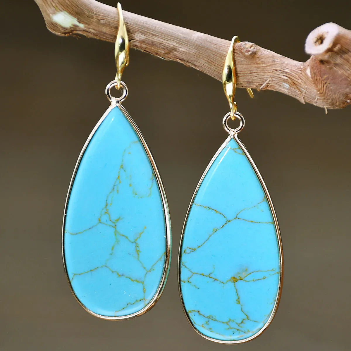 Close-up of long, polished tigereye stone drop earrings with a fishhook clasp on a neutral background.