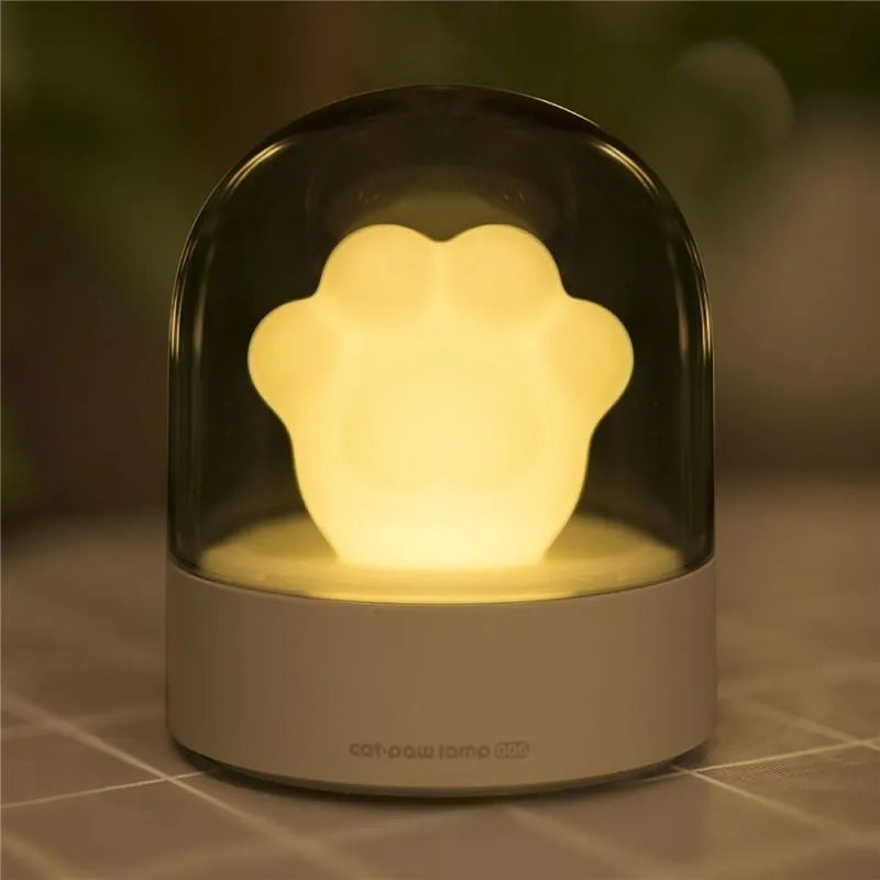 Grey cat paw shaped night light with USB port and button, glowing softly on a wooden desk.