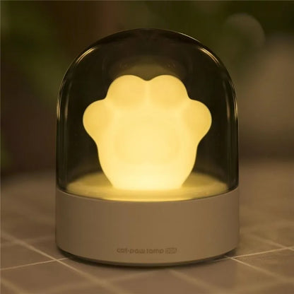 Grey cat paw shaped night light with USB port and button, glowing softly on a wooden desk.