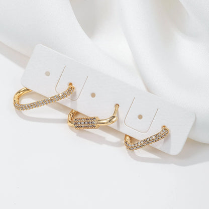 Three geometric copper ear clips with micro inlaid zircon in gold and white tones on a grey background.
