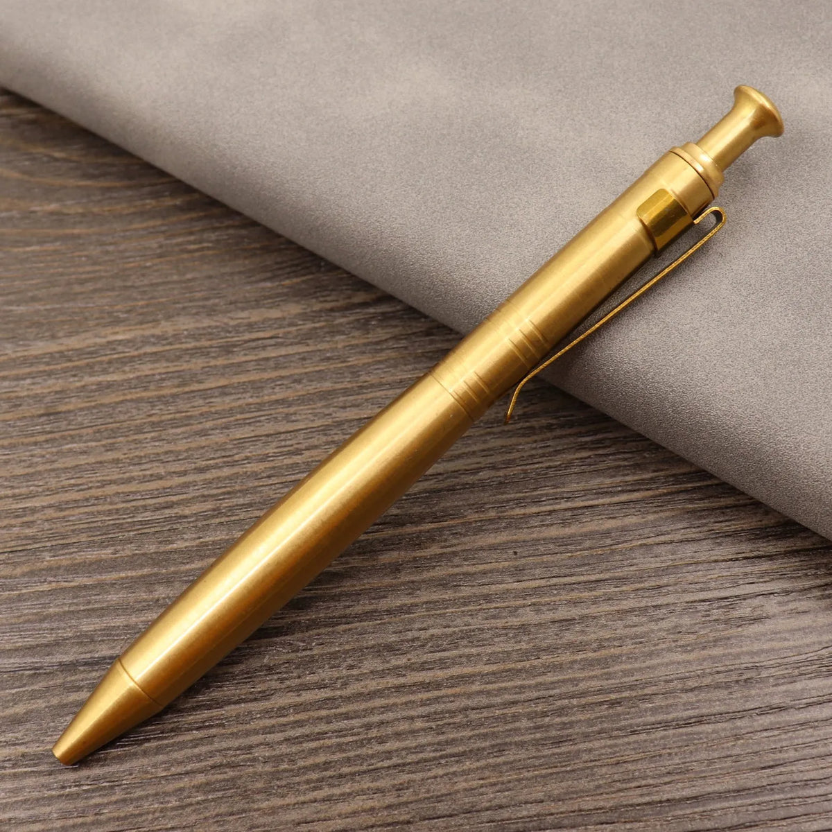 Brass tactical pen with press bolt mechanism showing cylindrical design and six ring details