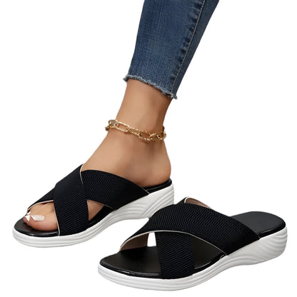 Women's black wedge-heel slippers with peep toe and cross-strap design on a thick rubber sole.
