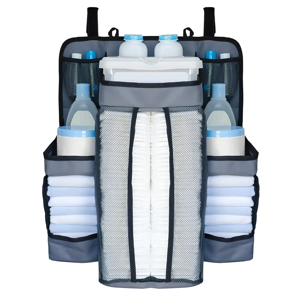 Grey baby nappy organiser attached to crib rail with Velcro straps, showing storage compartments for nappies and essentials