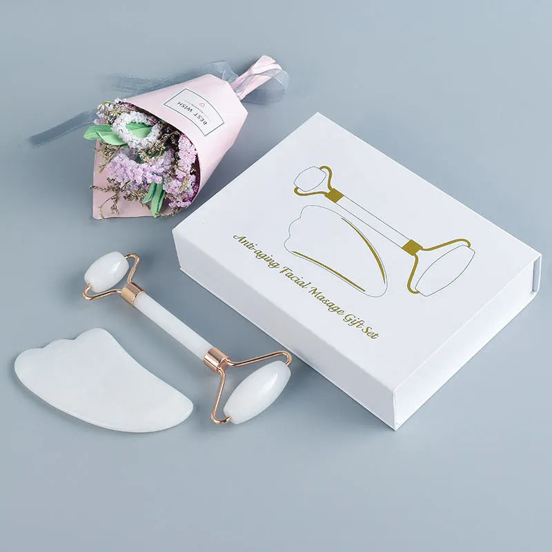 White jade facial roller with double heads and matching scraping board on dark surface