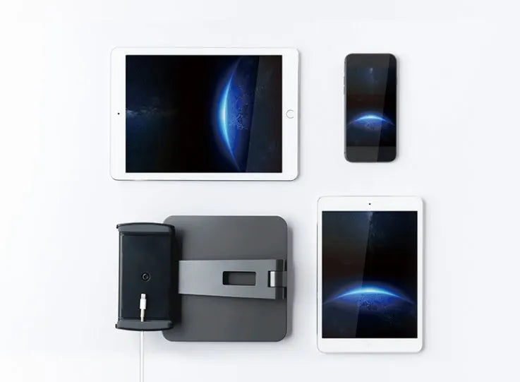 Silver foldable aluminium phone and tablet holder on a wooden desk, showing 360-degree rotation and silicone pads.