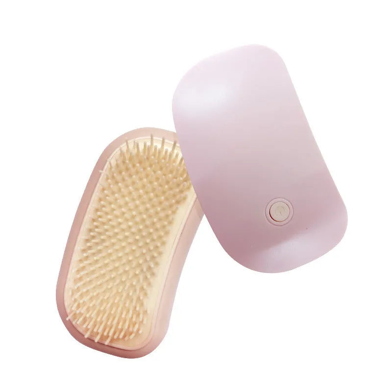 Pink Fuigarry handheld electric pet brush with soft teeth, placed on a carpet next to a cat.