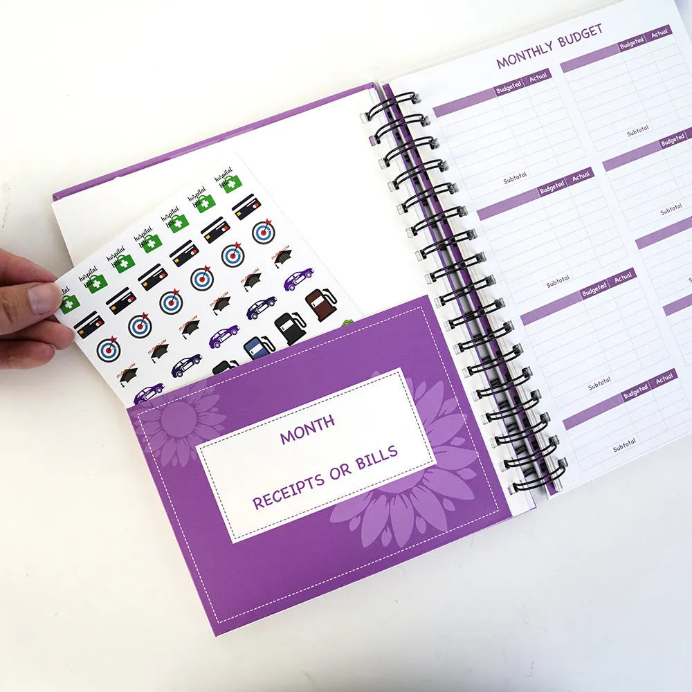 Purple A5 financial planning notebook with coil binding, showing monthly budget layout and included pen with stickers