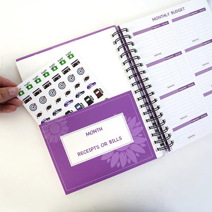 Purple A5 financial planning notebook with coil binding, showing monthly budget layout and included pen with stickers