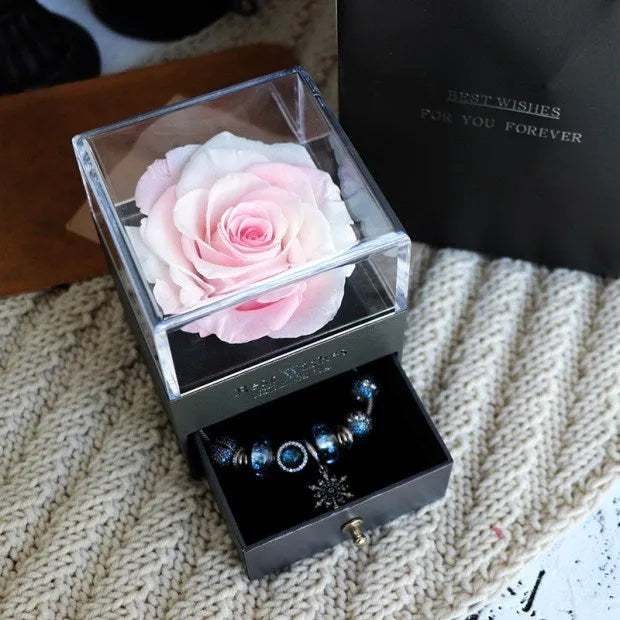 Blue and pink eternal flower gift box with roses and carnations on a table.