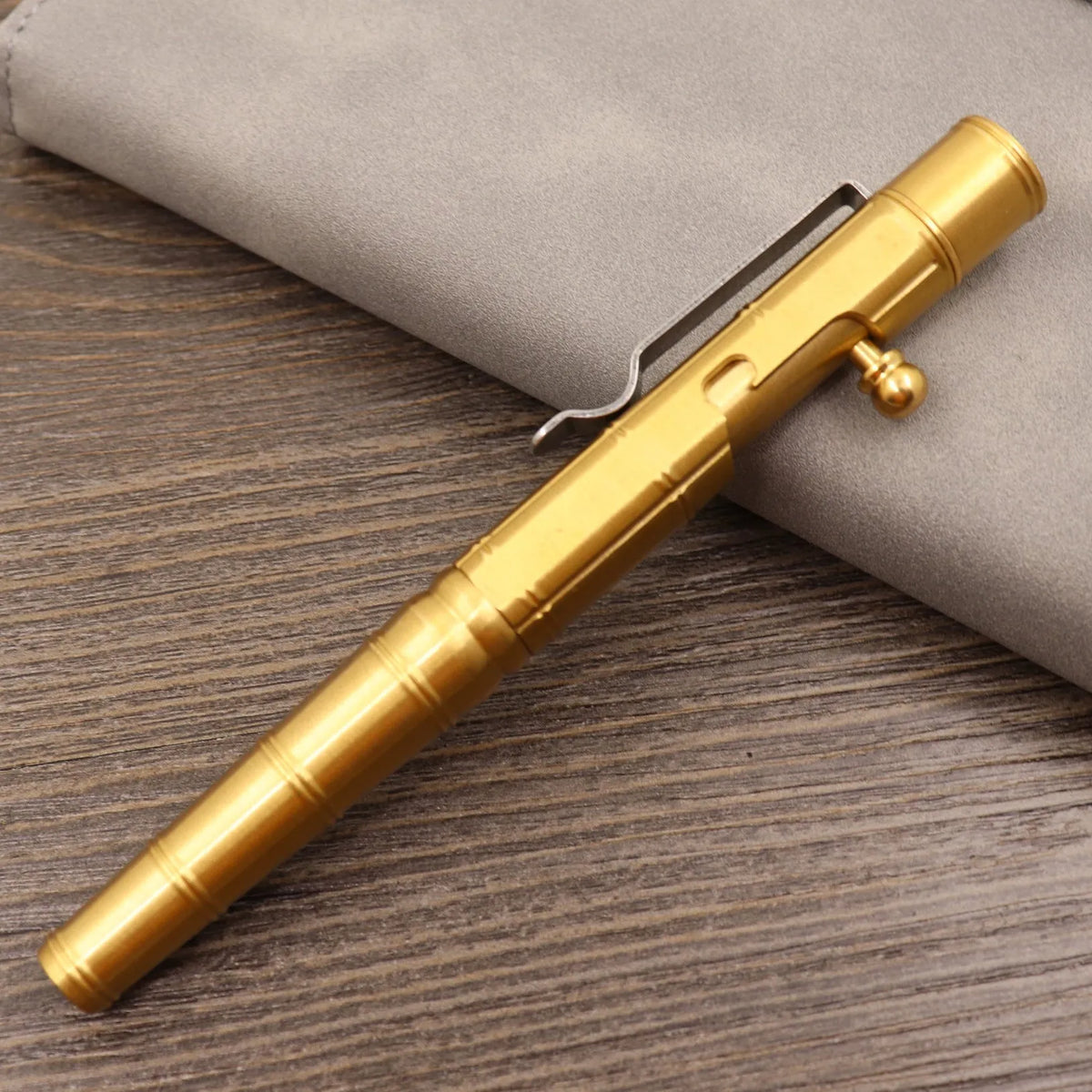 Brass tactical pen with press bolt mechanism showing cylindrical design and six ring details