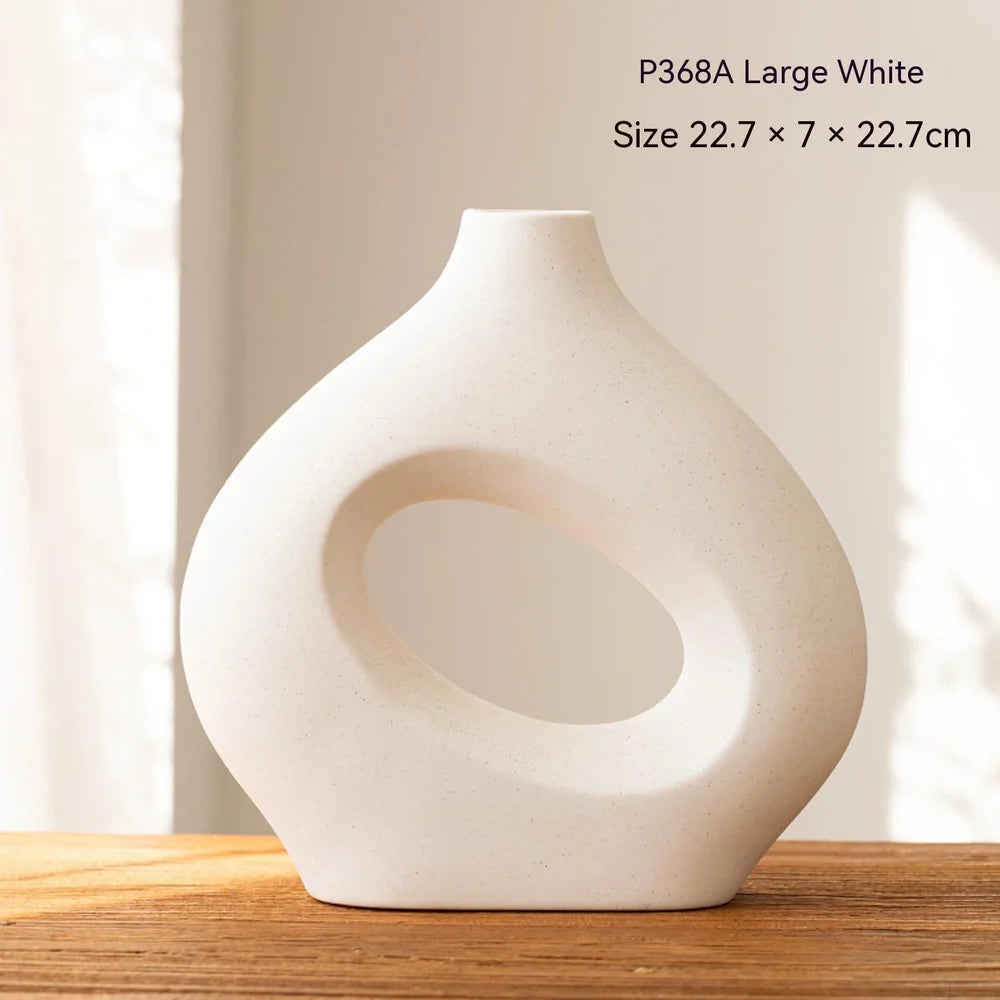 White ceramic circle vase with hand-painted coloured glaze on wooden table with dried flowers