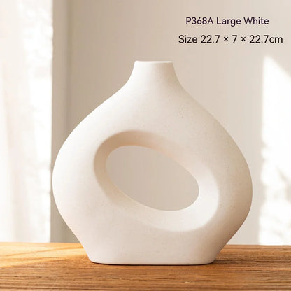 White ceramic circle vase with hand-painted coloured glaze on wooden table with dried flowers