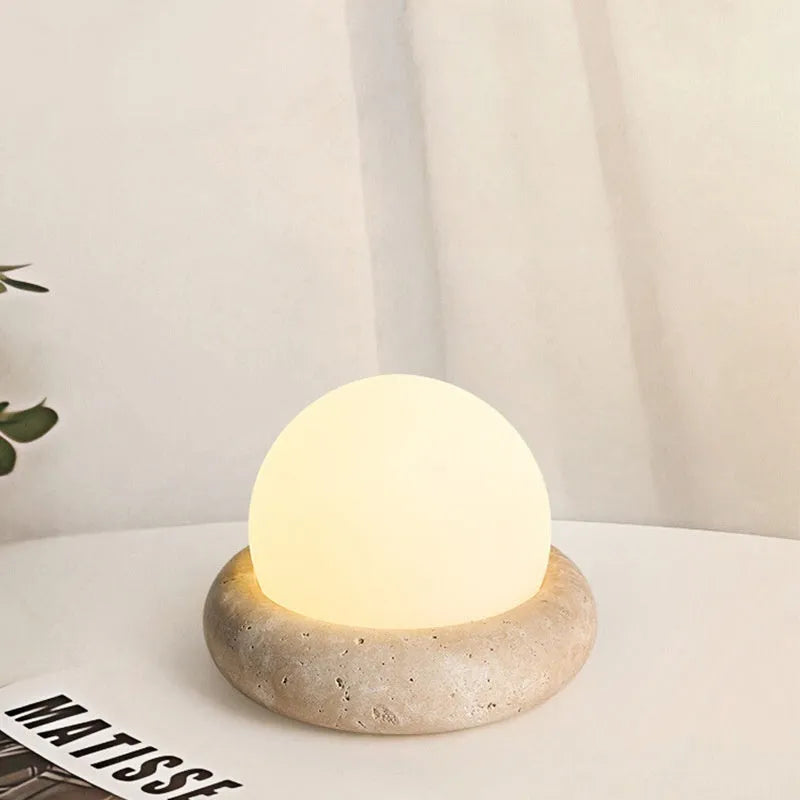 Modern white bedside night lamp with remote control on a wooden table.
