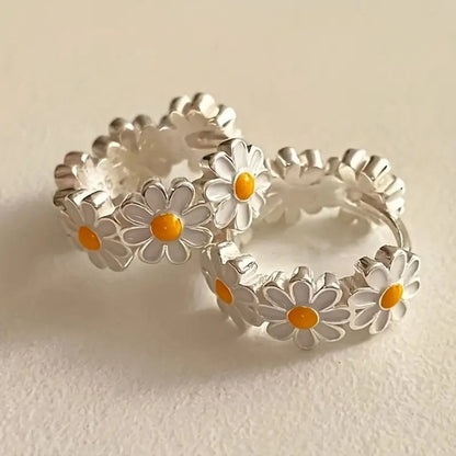 A pair of white daisy flower ring earrings with an inlaid gemstone in a platinum setting.