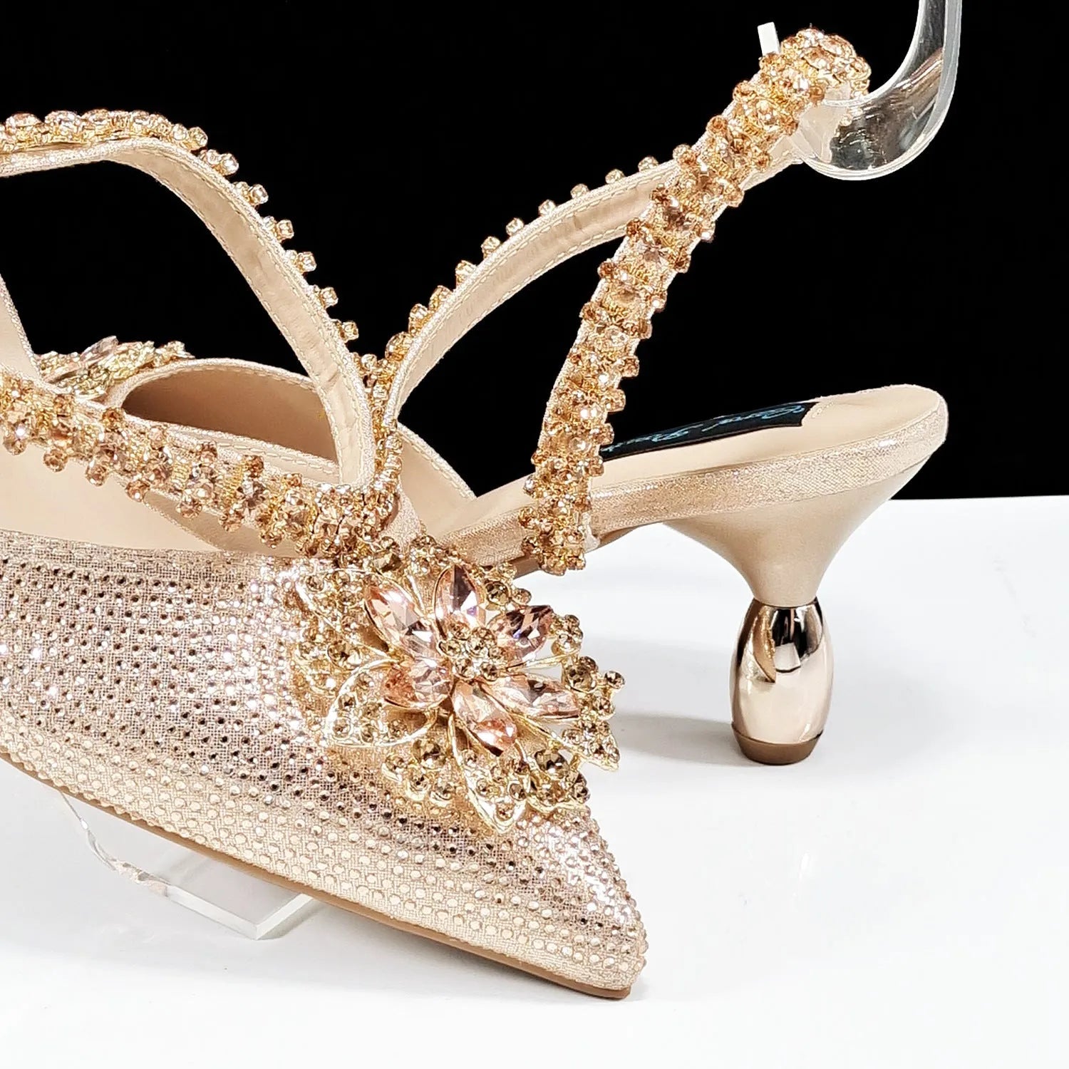 Women's black high-heel ankle strap shoes with floral rhinestone buckle and matching clutch bag on a neutral background