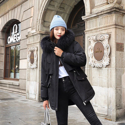 A model wearing a black down padded jacket with a fur-trimmed hood, standing outdoors in a snowy environment.