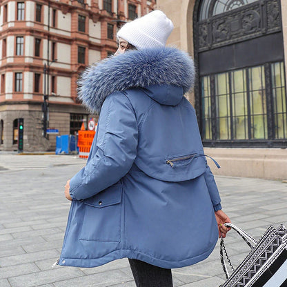 A model wearing a black down padded jacket with a fur-trimmed hood, standing outdoors in a snowy environment.