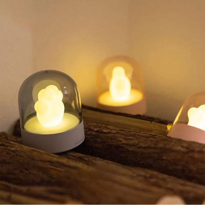 Grey cat paw shaped night light with USB port, shown on a wooden desk next to a charging cable.