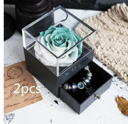 Blue and pink eternal flower gift box with roses and carnations on a table.