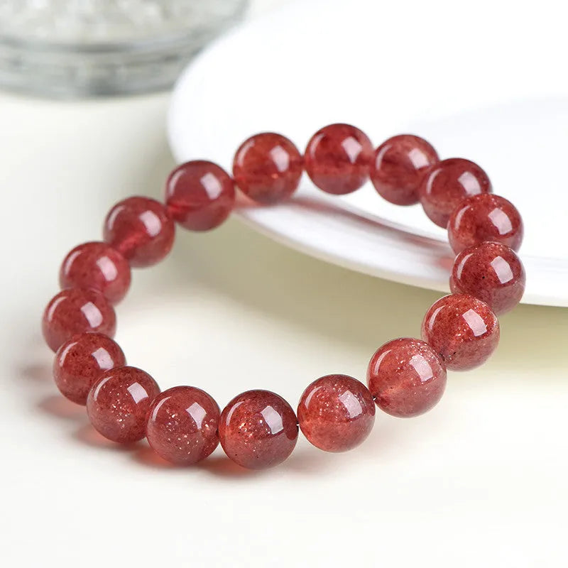 A polished strawberry quartz crystal bracelet in cherry red on a white background, showing geometric beads.