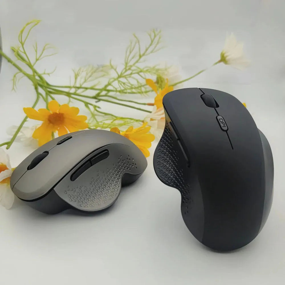 Compact grey wireless mouse with USB charging cable on a wooden desk next to a laptop.