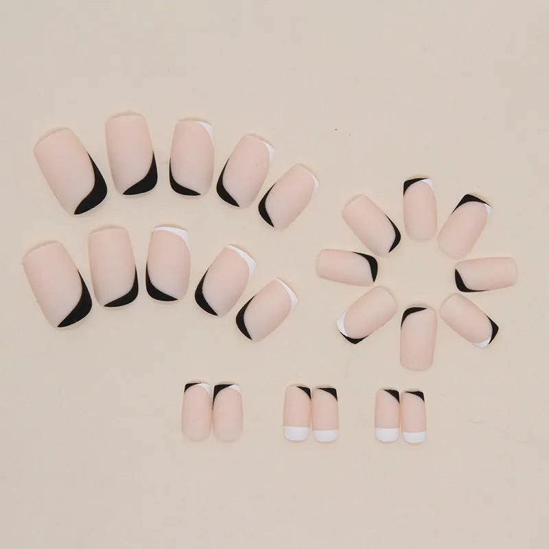 Set of 24 black and white frosted French tip fake nails with matte finish, laid out in size order.