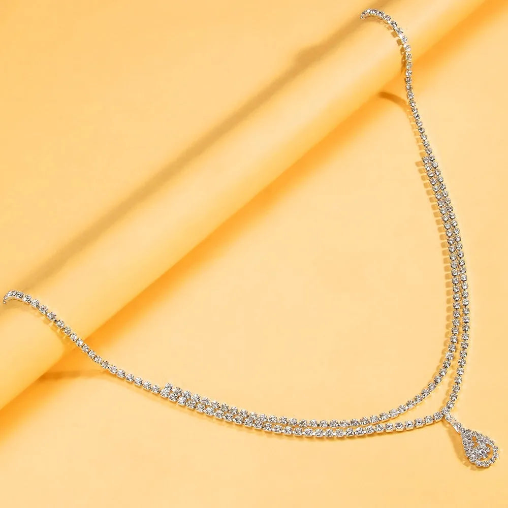 Gold water drop pendant waist chain with tassel detail and lobster buckle closure on white background