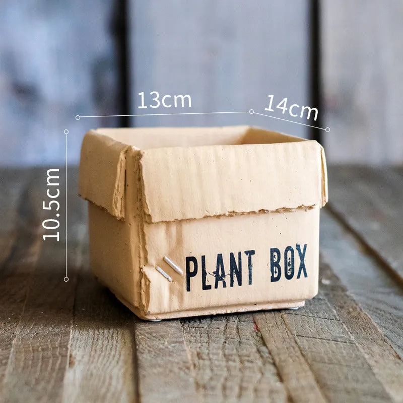Square cement planter with matte finish and drainage holes, next to a small green plant.