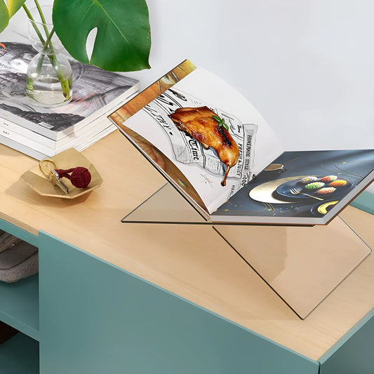 Clear acrylic X-shaped book display stand holding an open book on a desk.