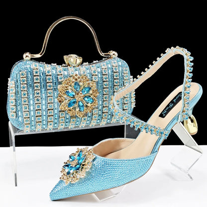 Women's black high-heel ankle strap shoes with floral rhinestone buckle and matching clutch bag on a neutral background