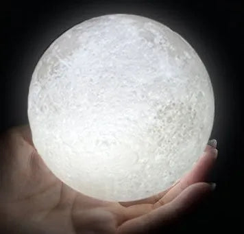 3D printed white moon lamp glowing on a wooden stand, showing detailed crater texture on its surface.