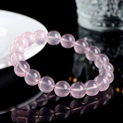 A polished natural starlight crystal round bead bracelet in pink, showing different size options on a wrist.