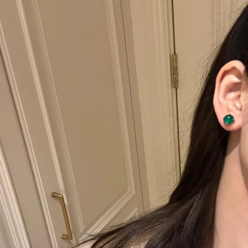 Close-up of a Chinese retro style stud earring with a round green chalcedony stone in a four-claw copper setting.